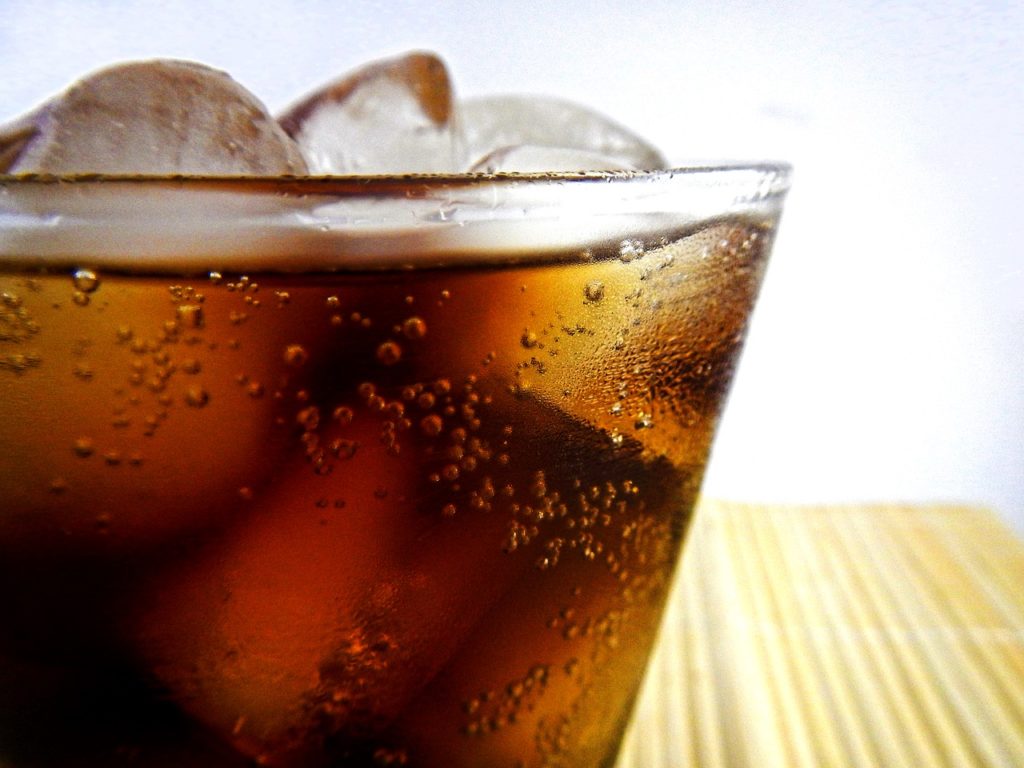 Brown colored soda in a glass with ice and bubbles